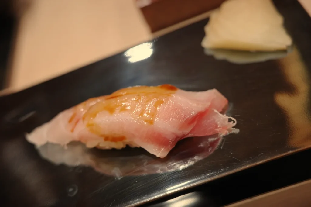 A piece of sushi on a black plate, accompanied by a slice of pickled ginger.