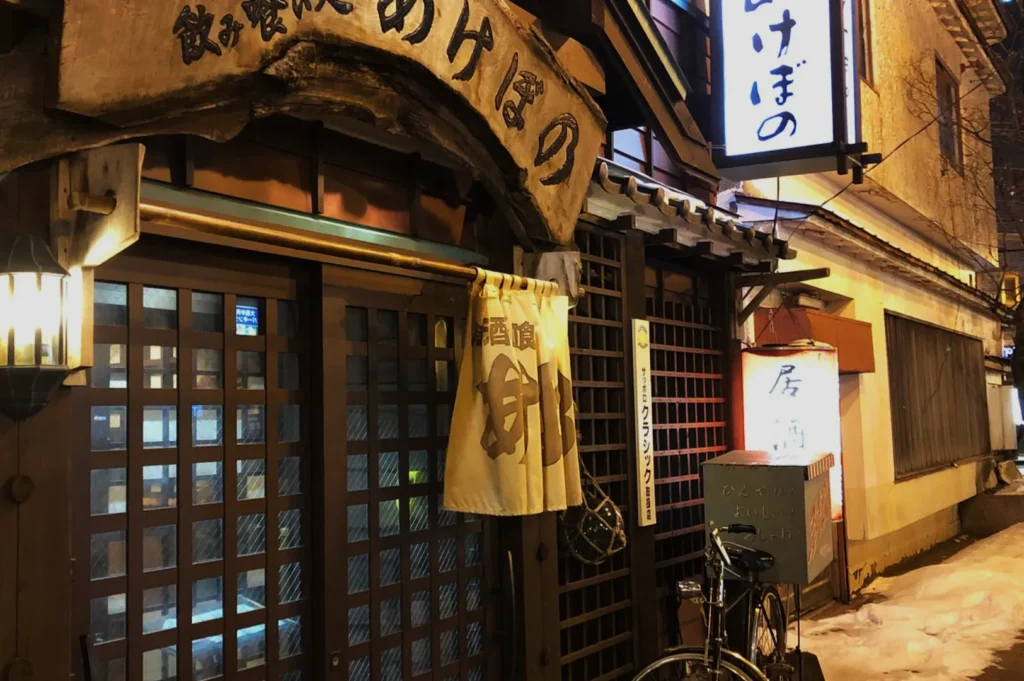 A traditional Japanese restaurant exterior with a sign and lanterns, featuring a bicycle parked outside.