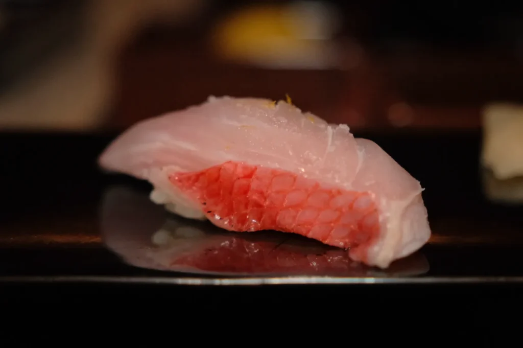 A piece of sushi with pink fish, presented on a dark plate.