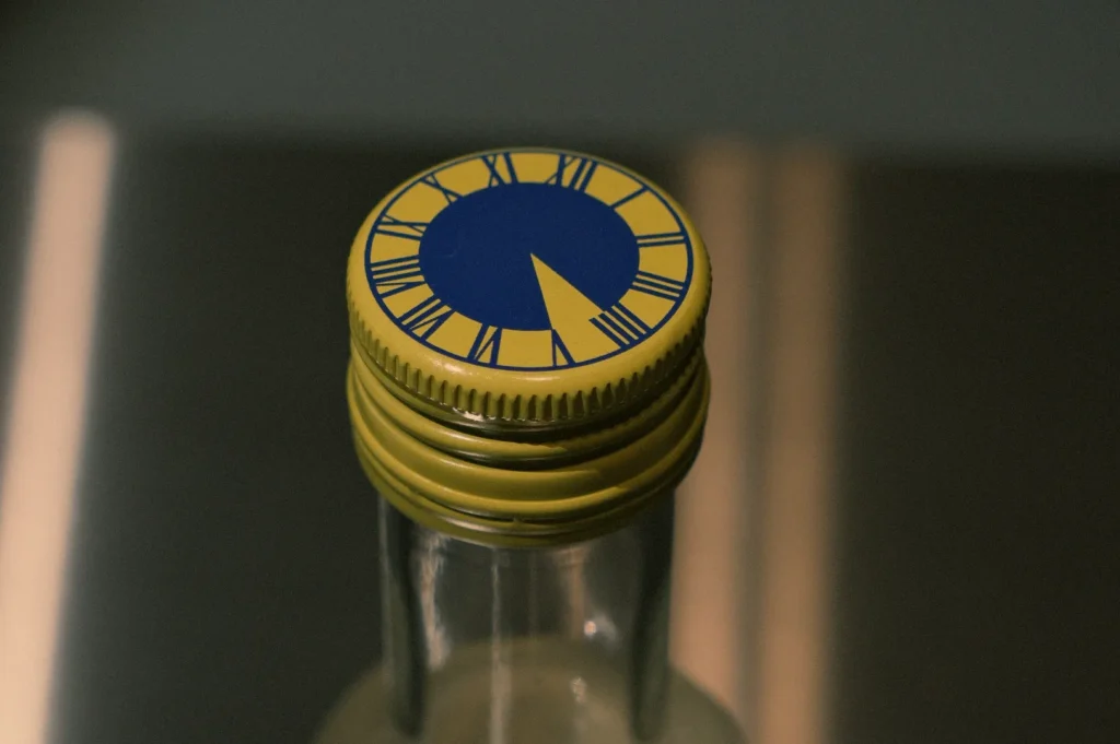 A close-up of the cap of a bottle with a design featuring a blue clock face and yellow background.