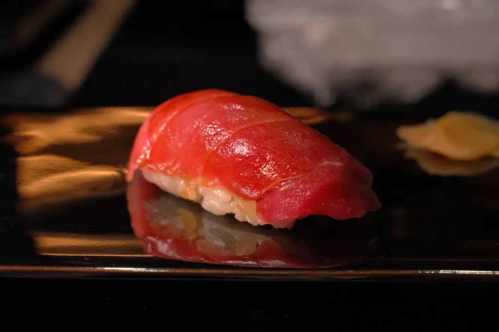 A piece of sushi with a vibrant red tuna topping on a dark plate.