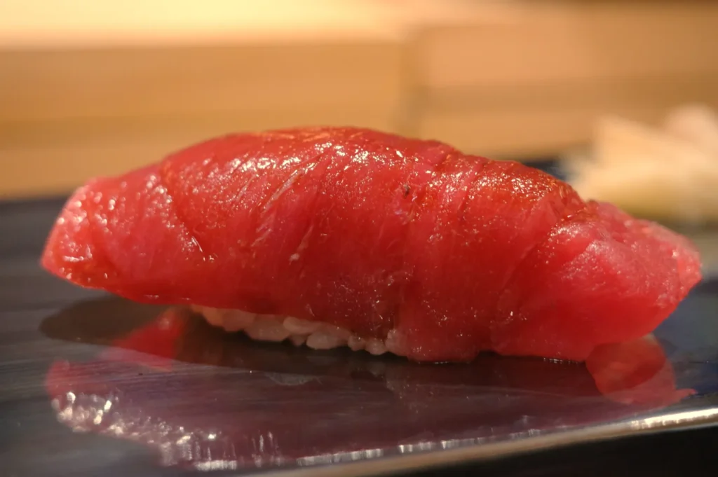 A piece of sushi with a slice of red tuna atop a small mound of rice.