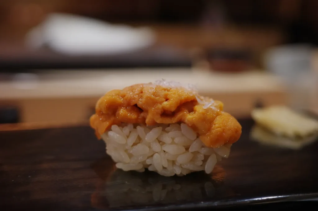 A piece of sushi topped with orange sea urchin (uni) on a bed of vinegared rice, set on a dark wooden surface.