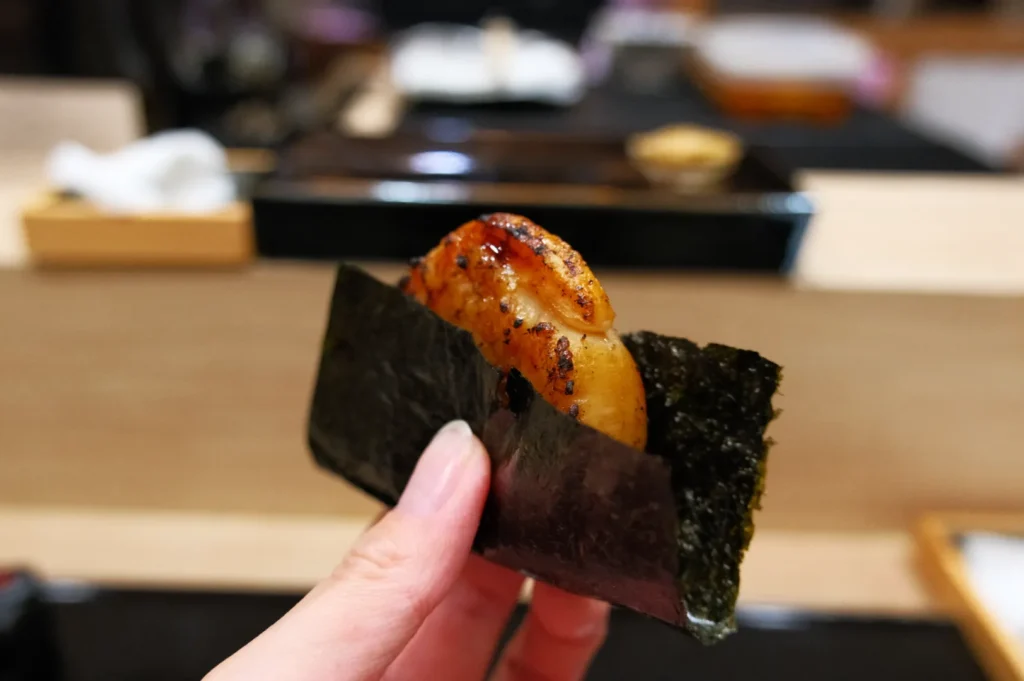 A piece of sushi held in hand, featuring grilled seafood wrapped in seaweed.