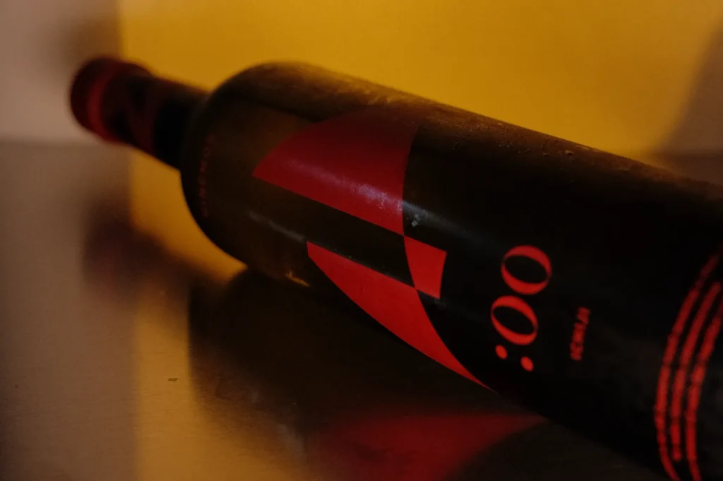 A dark wine bottle lying on its side with a red label featuring a stylized ":00" design.