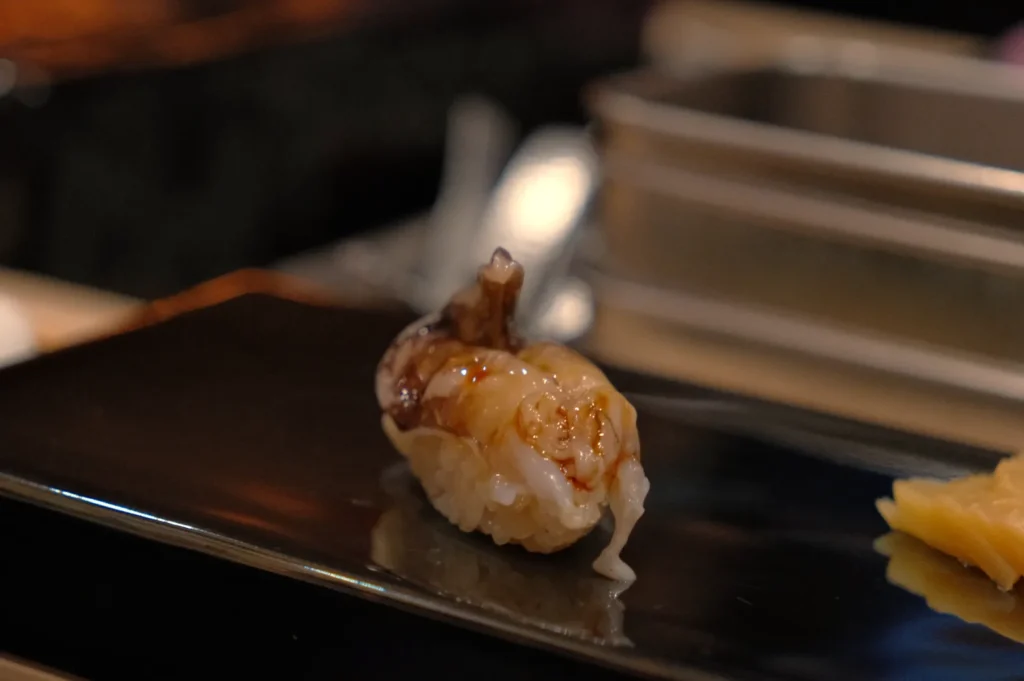 A piece of sushi on a black plate, featuring a clam with a glistening surface.