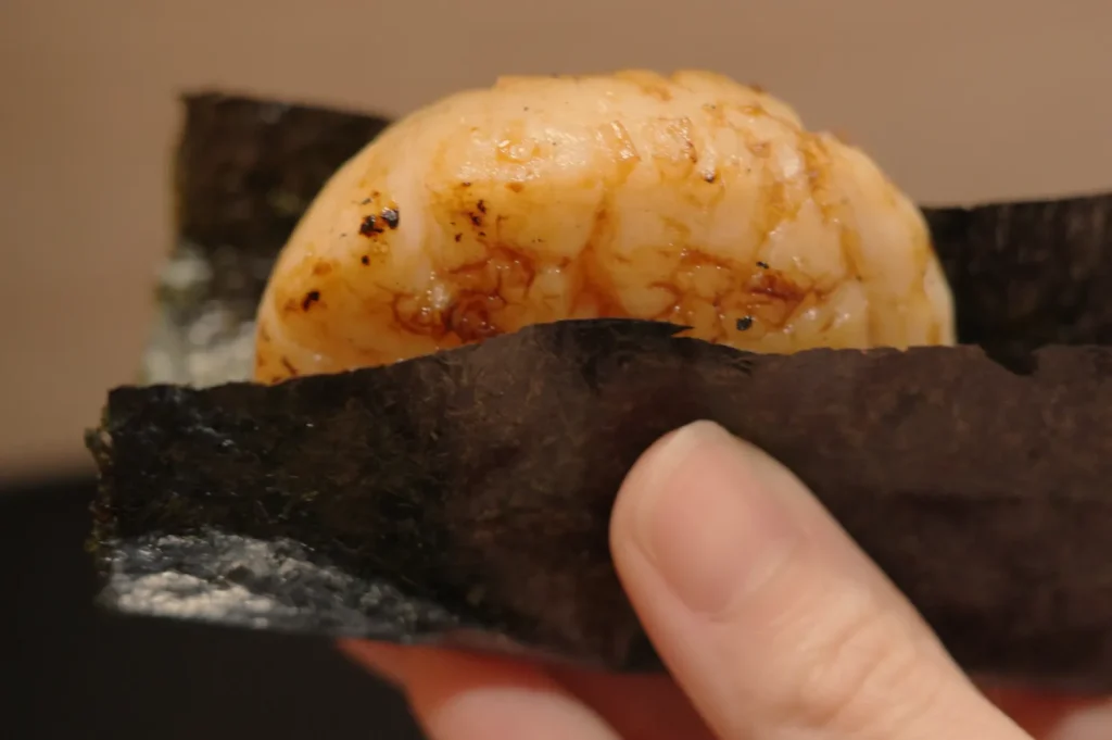 A hand holding a piece of sushi wrapped in seaweed.