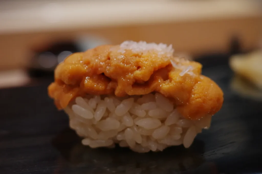 A piece of sushi topped with orange sea urchin (uni) on a small mound of rice.