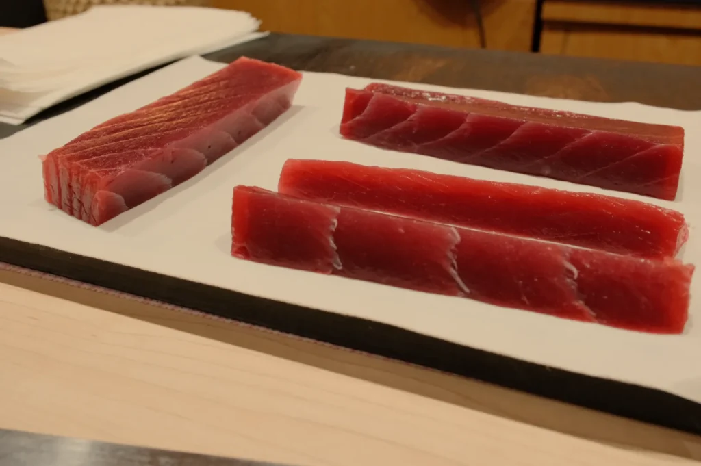 Three pieces of sushi-grade tuna displaying different cuts and colors on a white plate.
