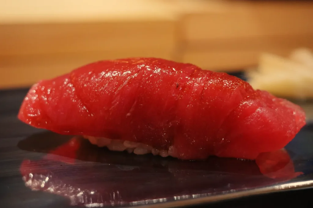 A piece of sushi featuring a slice of red tuna atop a small mound of rice.