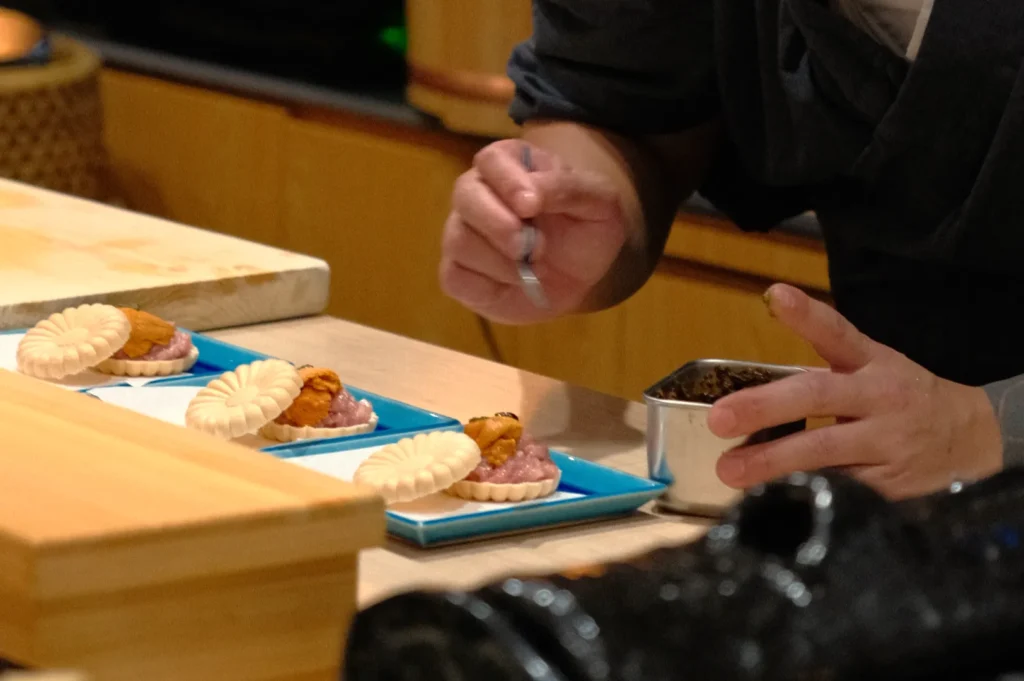 A chef preparing small, intricate dishes on blue plates, with a focus on plating and garnishing.
