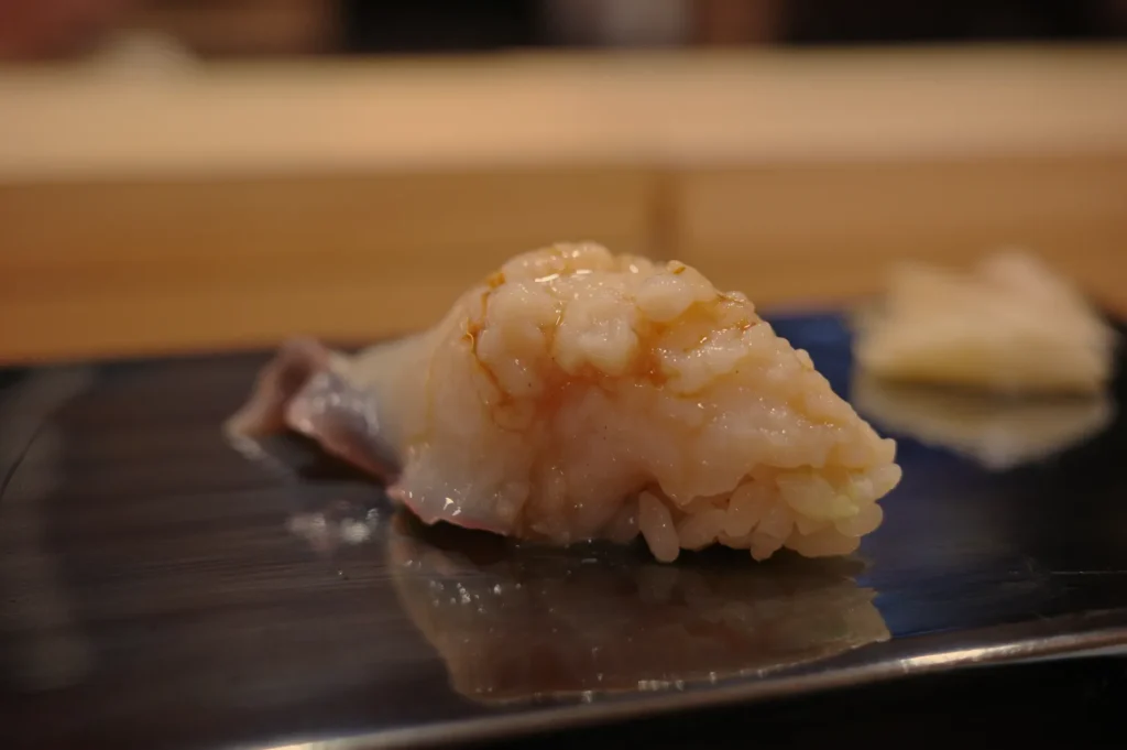 A piece of sushi on a metal plate, with a focus on the rice and the topping, which appears to be raw fish.