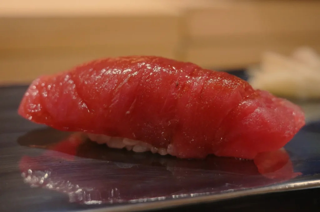 A piece of sushi featuring a slice of red tuna on top of vinegared rice.