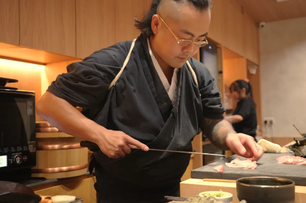 A chef in traditional attire skillfully prepares sushi at a counter, focusing on his work.