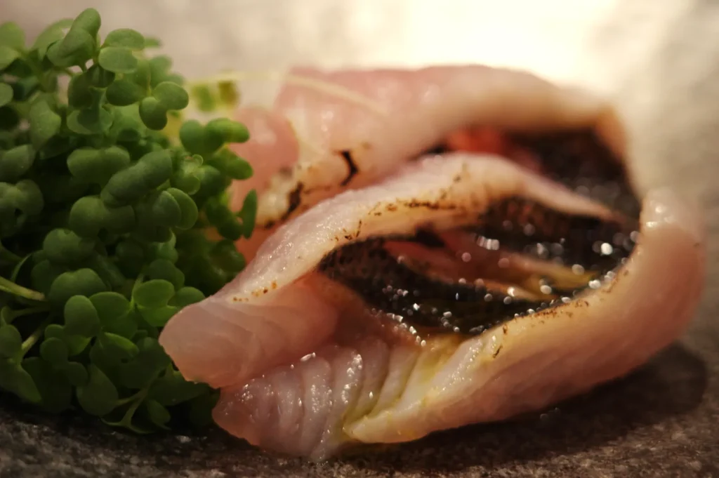 A piece of fish served with a garnish of green herbs on a textured plate.