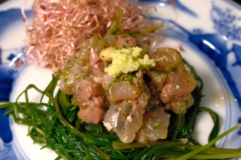 A plate of seaweed salad topped with chopped fish and a dollop of wasabi, accompanied by a mound of pink shiso sprouts.