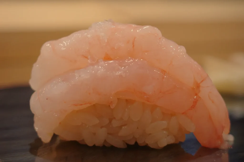 A piece of sushi with a translucent pink seafood topping over a small mound of seasoned rice.