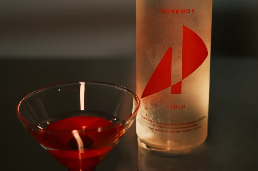 A bottle of beverage with a minimalist design next to a glass containing a red drink.
