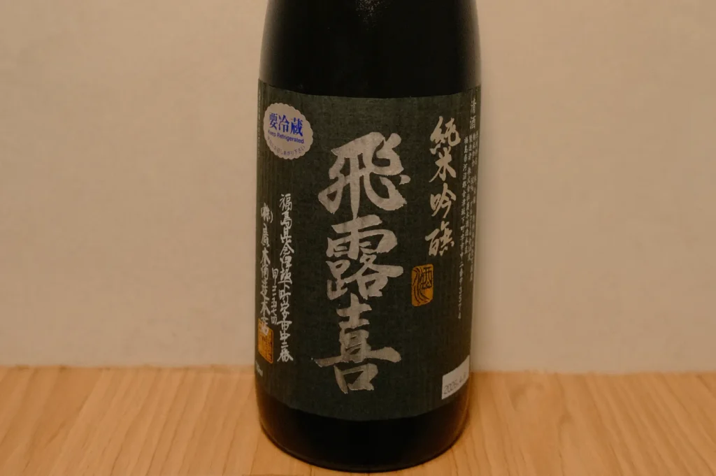 A bottle of sake with a black label featuring white and gold Japanese text.