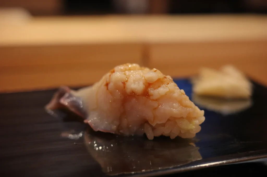 A piece of sushi on a black plate, featuring a mound of rice topped with a shiny, pale seafood.
