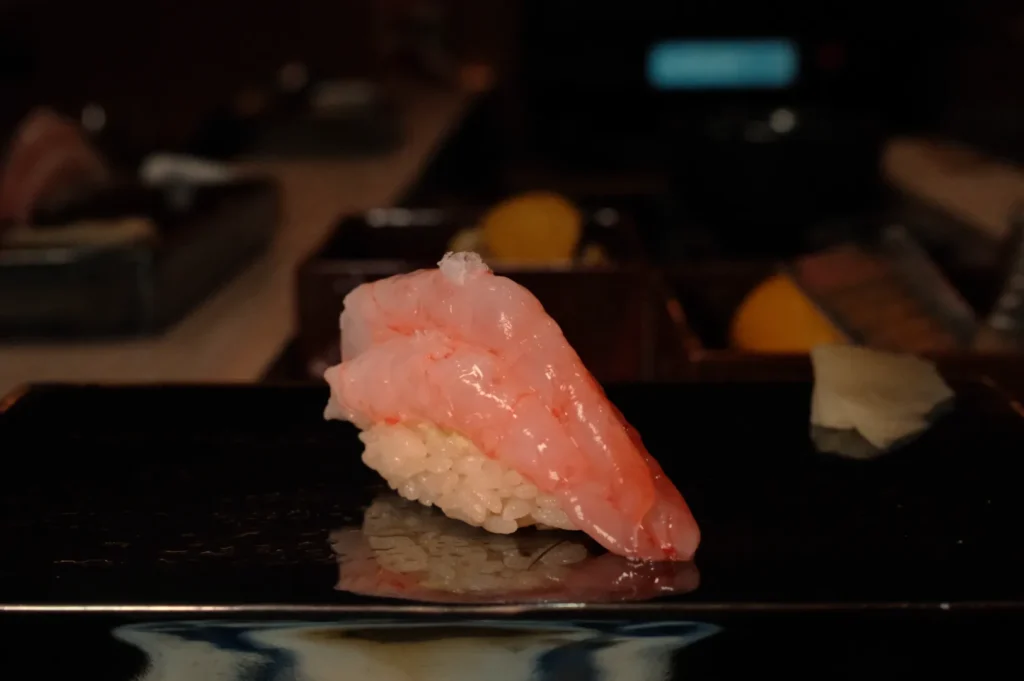 A piece of sushi topped with a pink piece of fish on a black plate.