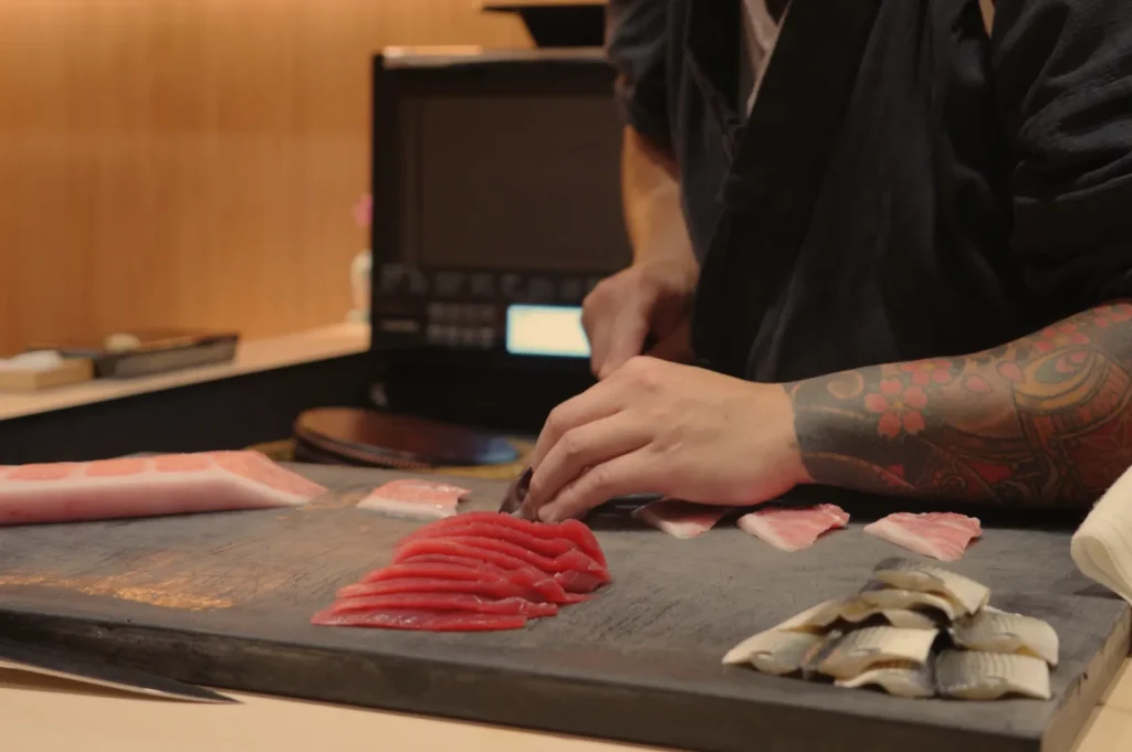 A sushi chef slicing fish on a wooden board, with various pieces of sashimi arranged neatly.