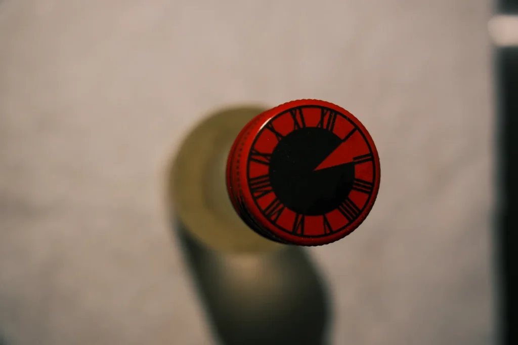 A close-up view of the top of a bottle with a red cap featuring clock-like markings.