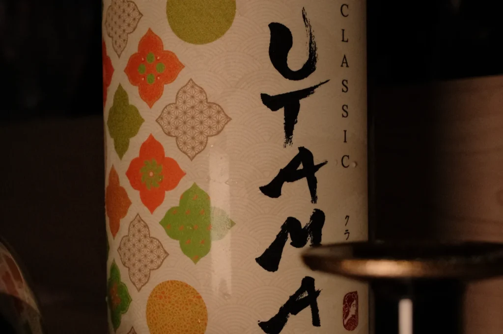 A close-up of a decorative bottle labeled "UTAMA CLASSIC" with floral patterns in orange, green, and beige against a light-colored background.