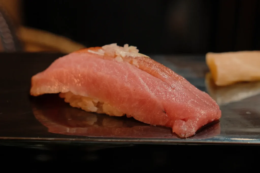A piece of sushi featuring a slice of pink tuna atop a small mound of rice.