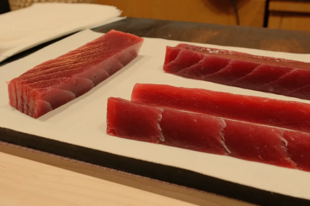Three pieces of red tuna sashimi laid out on a white plate, showcasing different cuts of the fish.