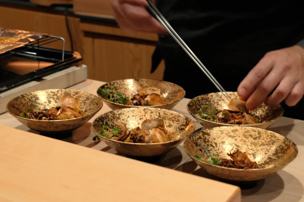 A person using chopsticks to plate food in decorative gold bowls.