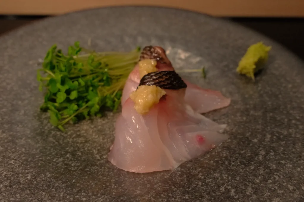 Slices of sushi atop a gray plate, accompanied by a small pile of microgreens and a dab of wasabi.