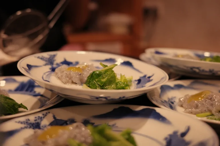 A close-up view of plates filled with food, featuring small portions of a translucent dish accompanied by green leafy vegetables.