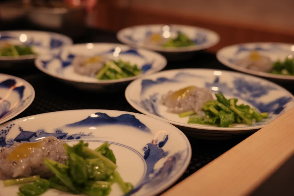A set of plates featuring a dish with small portions of food, including a green vegetable and a smear of a sauce or puree, arranged aesthetically.