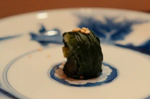A small piece of green food on a blue and white plate.