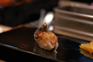 A piece of sushi on a black plate, featuring shrimp.