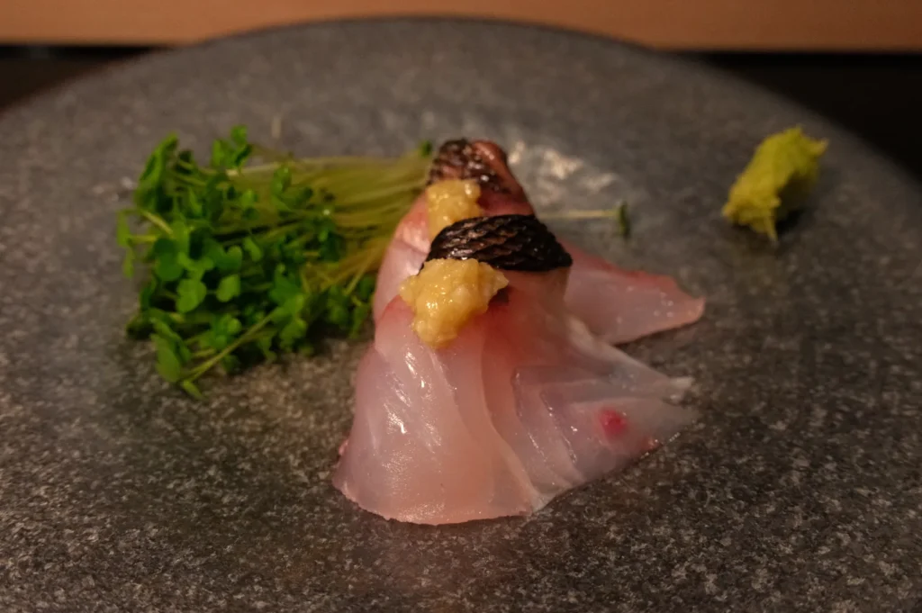 A plate of sushi featuring slices of fish, garnished with wasabi and fresh greens.