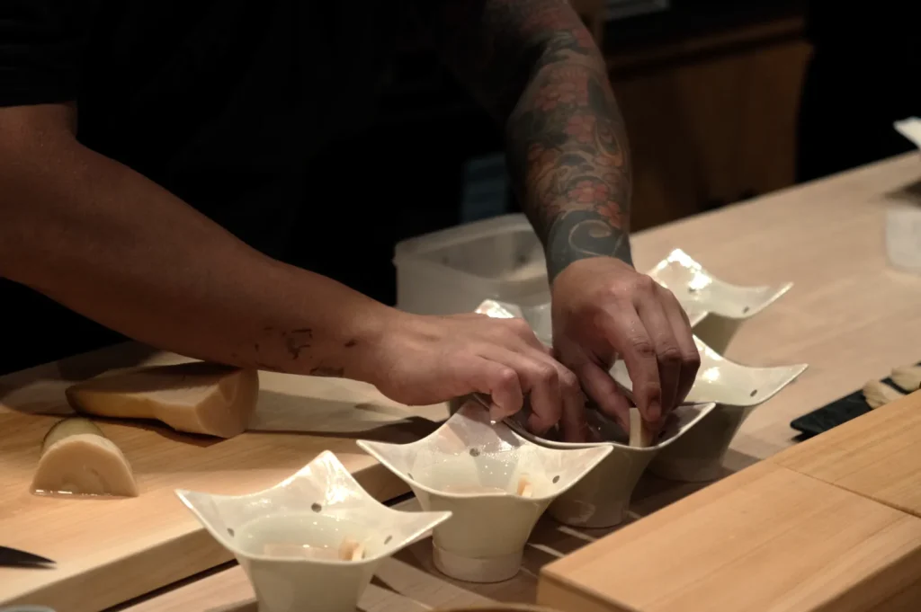 Chef Masa arranging ingredients in small, ornate bowls on a countertop.