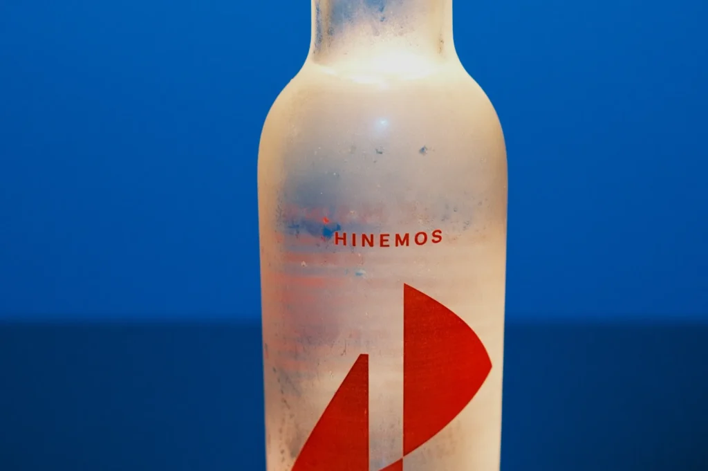 A frosted glass bottle with a red logo and the text "Hinemos" on a blue background.