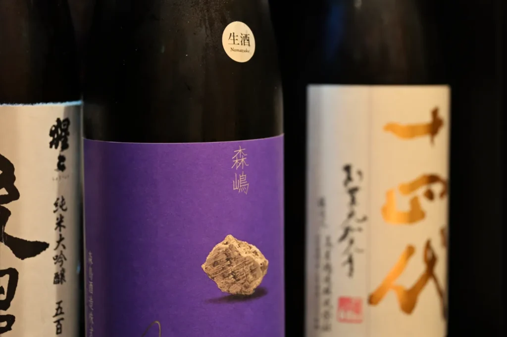 Bottles of sake with distinct labels, including a purple label with a stone and traditional Japanese characters.