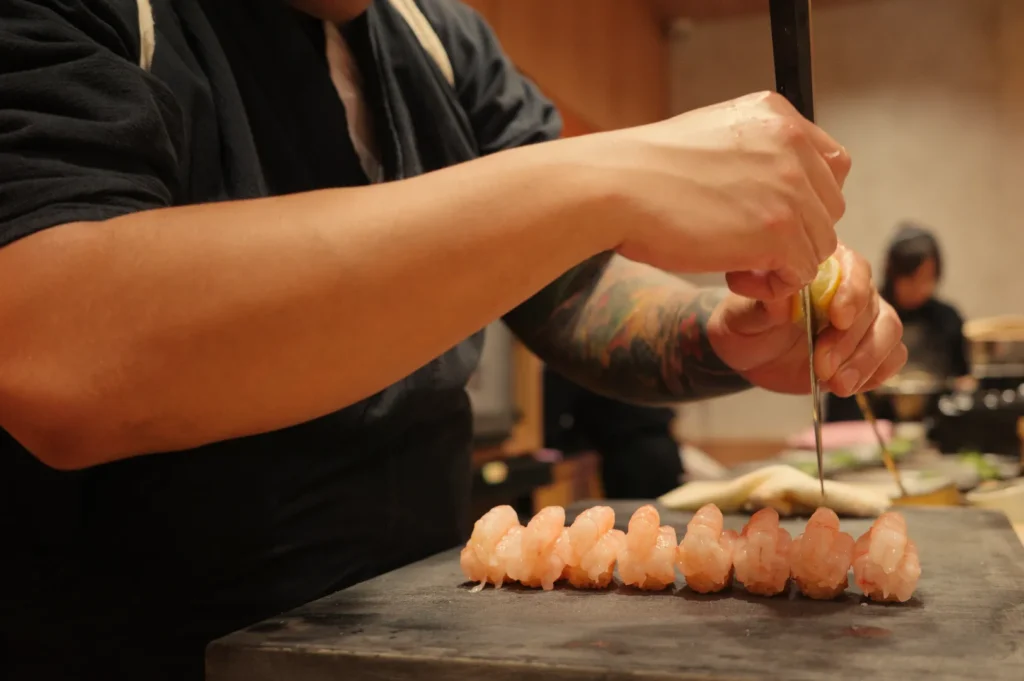 Chef Masa carefully prepares sushi, slicing fish with precision on a wooden cutting board.