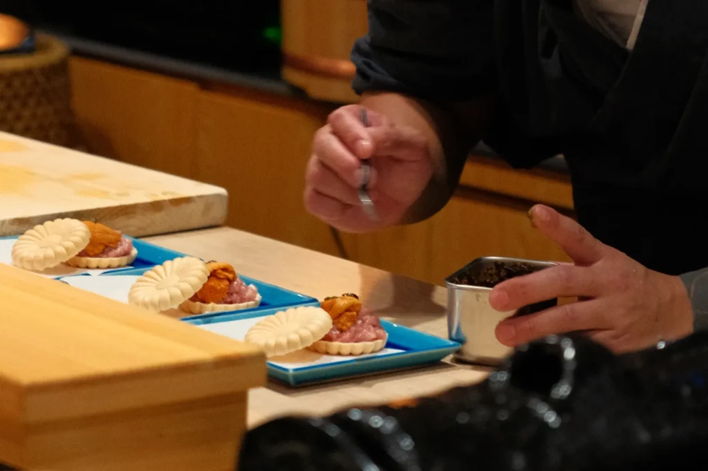 Chef Masa carefully plating sushi on small blue plates in a kitchen setting.