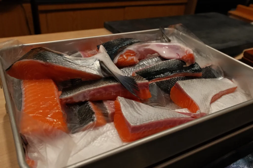 A tray of various types of sliced fish, including salmon, arranged in a metal container.