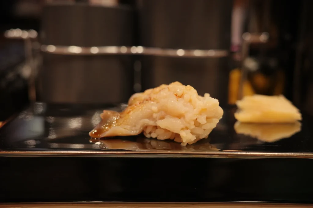 A piece of sushi served on a black plate, accompanied by a small portion of pickled ginger.