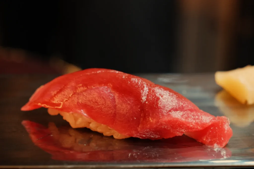 A piece of sushi with a bright red slice of tuna on top of a small mound of rice.