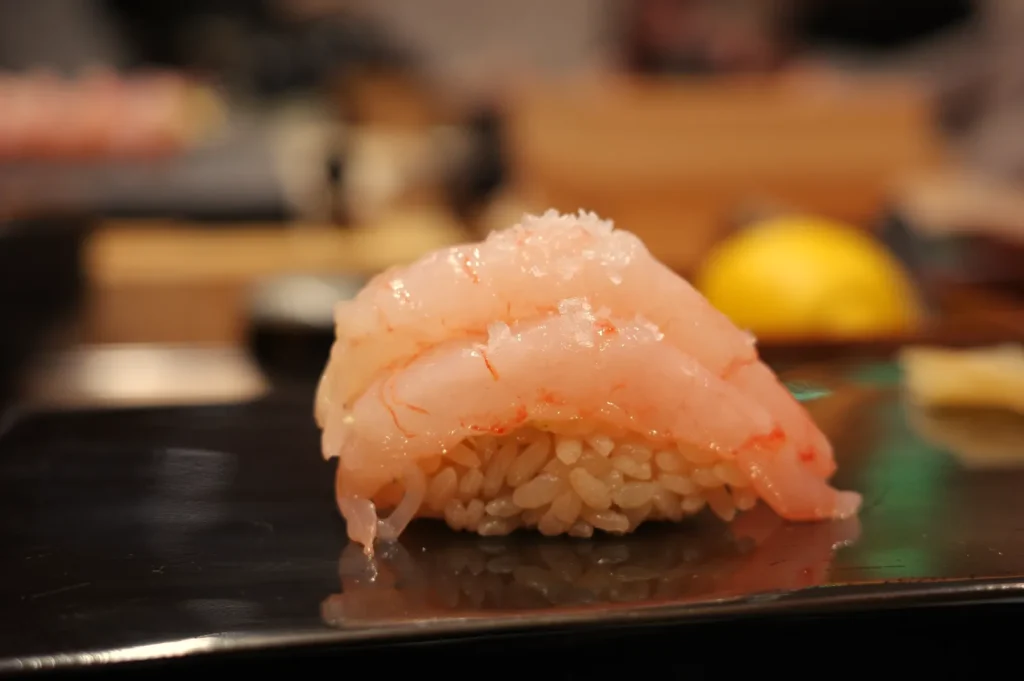 A piece of sushi with pink seafood layered on top of rice, served on a black plate.