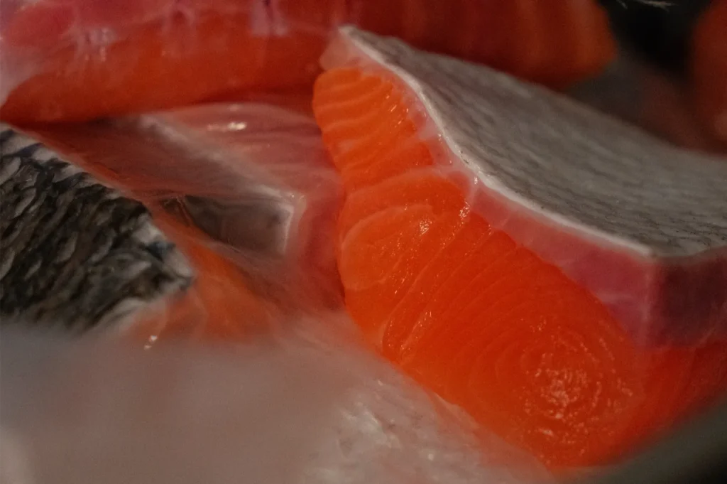 Fresh salmon fillets with varying textures and colors, showing a close-up of the flesh and skin.