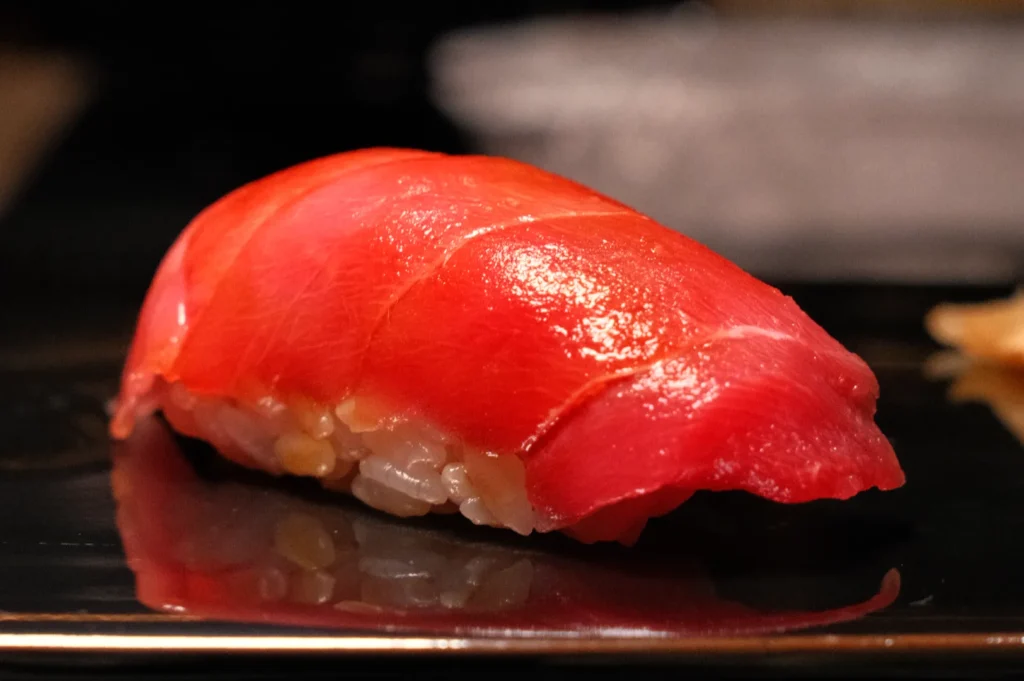 A piece of sushi, specifically nigiri, featuring a slice of raw tuna on top of vinegared rice.