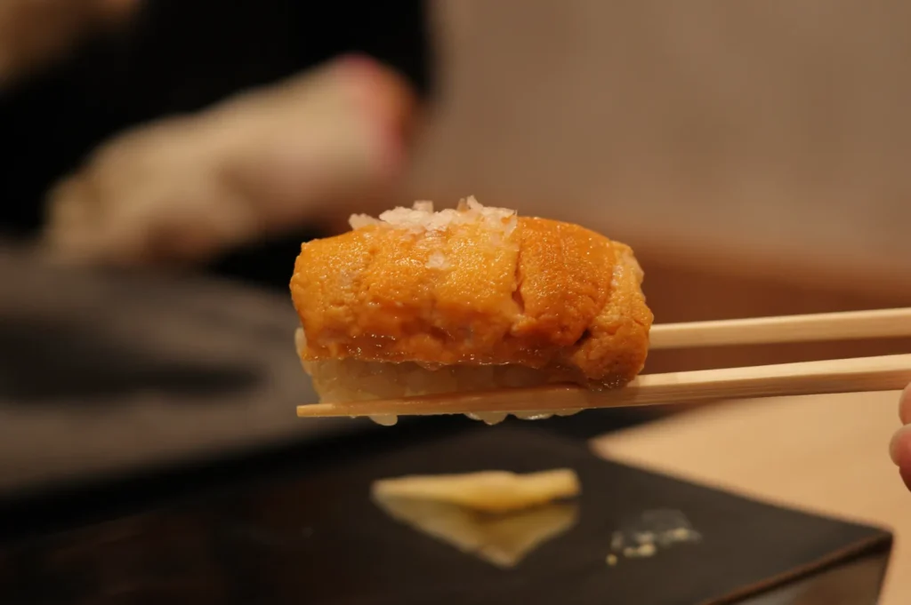 A piece of sushi, specifically uni (sea urchin), being held with chopsticks.