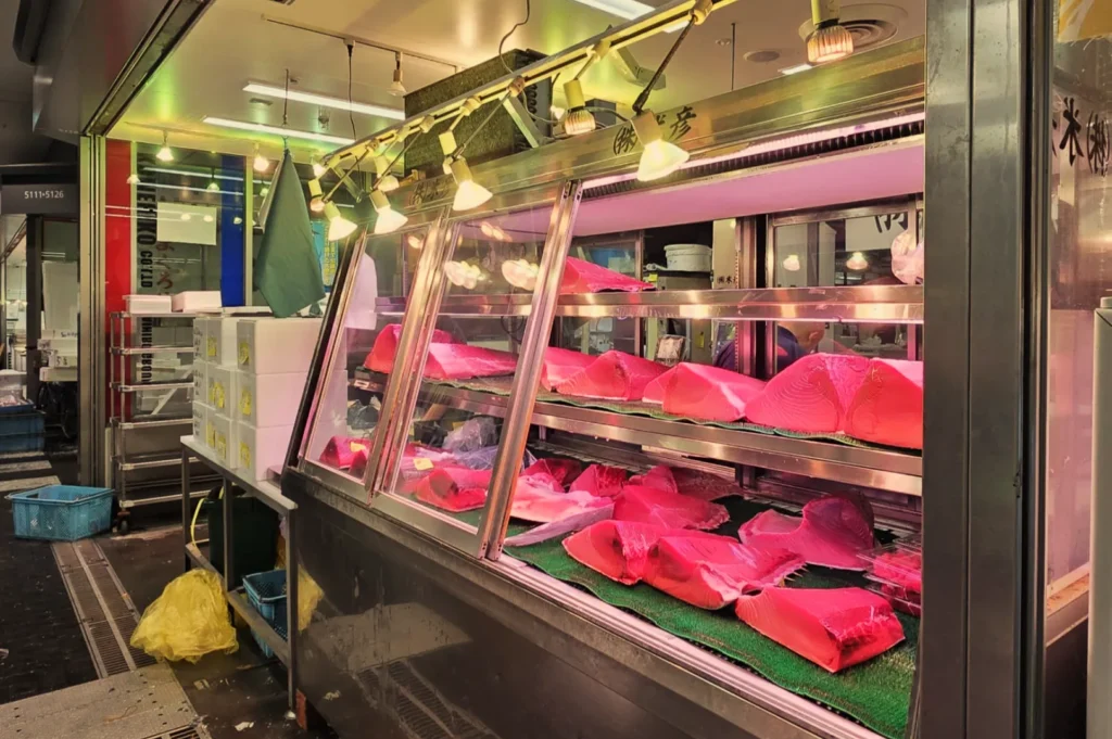 A fish market display featuring various cuts of pink tuna, illuminated under bright lights.